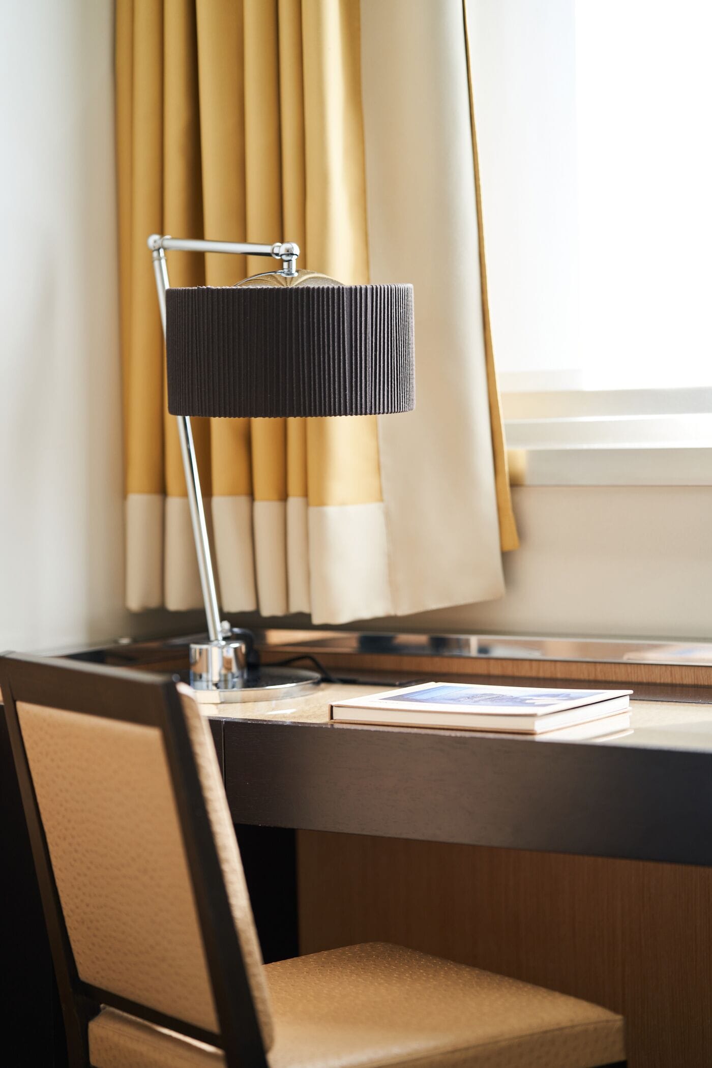 Een bureau met een lamp, een stoel en een raam met gordijnen.