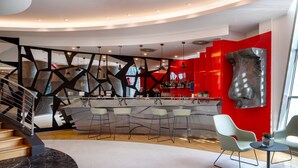 A modern bar area with a curved counter, bar stools, and a red accent wall. - UNA Hotels Malpensa (Cerro Maggiore)