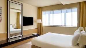 A hotel room with a large bed, a flat-screen TV mounted on the wall, a bedside table with a lamp, and a window with curtains. - UNA Hotels Malpensa (Cerro Maggiore)
