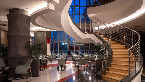 A modern hotel lobby with a spiral staircase, marble flooring, and a large column. - UNA Hotels Malpensa (Cerro Maggiore)