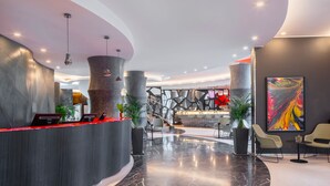 A modern lobby with a curved reception desk, seating area, and a large abstract painting. - UNA Hotels Malpensa (Cerro Maggiore)