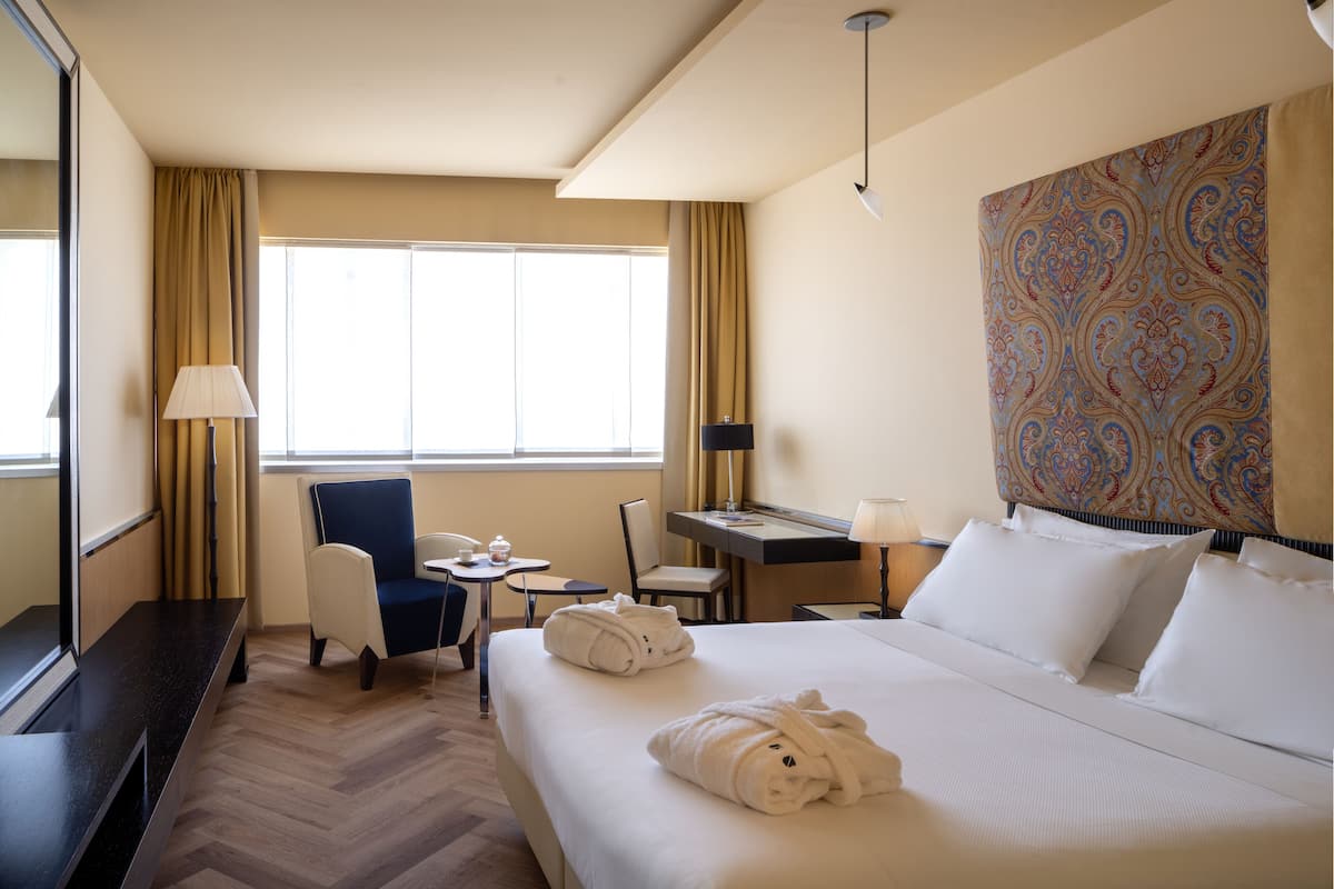 Una habitación de hotel con una cama, dos sillas, un escritorio con lámpara, un teléfono y una ventana con cortinas.