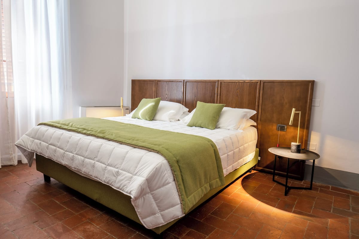 A neatly made bed with a green and white quilt, a wooden headboard, and a bedside table with a lamp.
