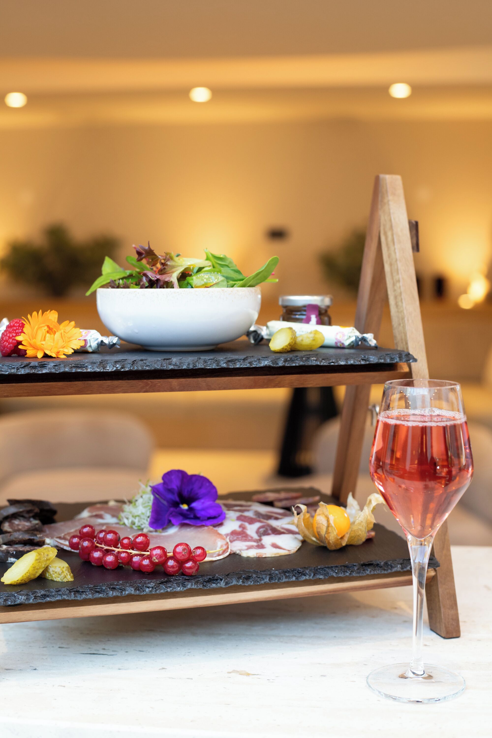 A dining setup with a salad bowl, fruits, and a wine glass on a black slate table.