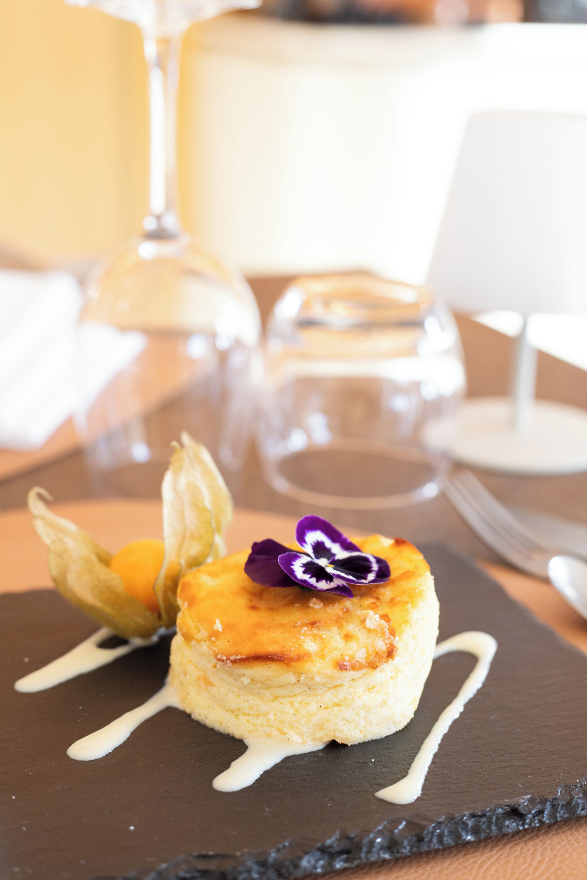 Un dessert servi sur une assiette en ardoise, nappé d’une sauce, accompagné d’un verre de vin et d’une bougie blanche en arrière-plan.
