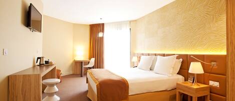 A hotel room with a bed, bedside table, lamp, desk, chair, and a TV mounted on the wall.