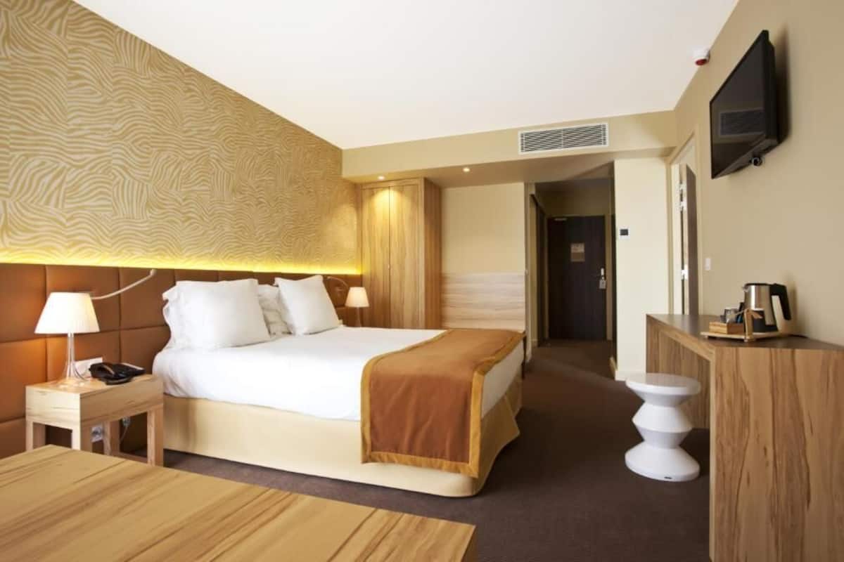 A hotel room with a large bed, bedside tables, a desk, and a television.