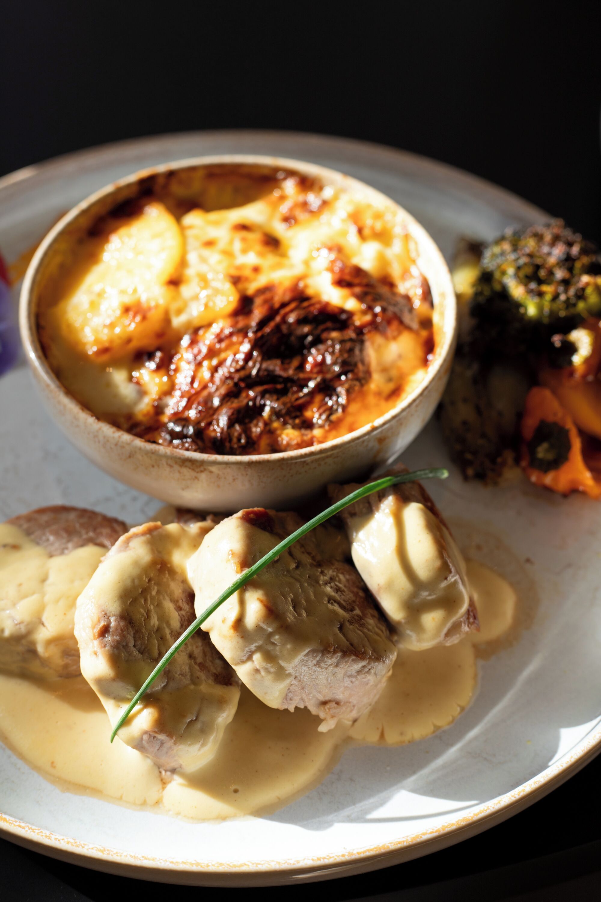 A plate with a creamy sauce, a baked dish, and vegetables.