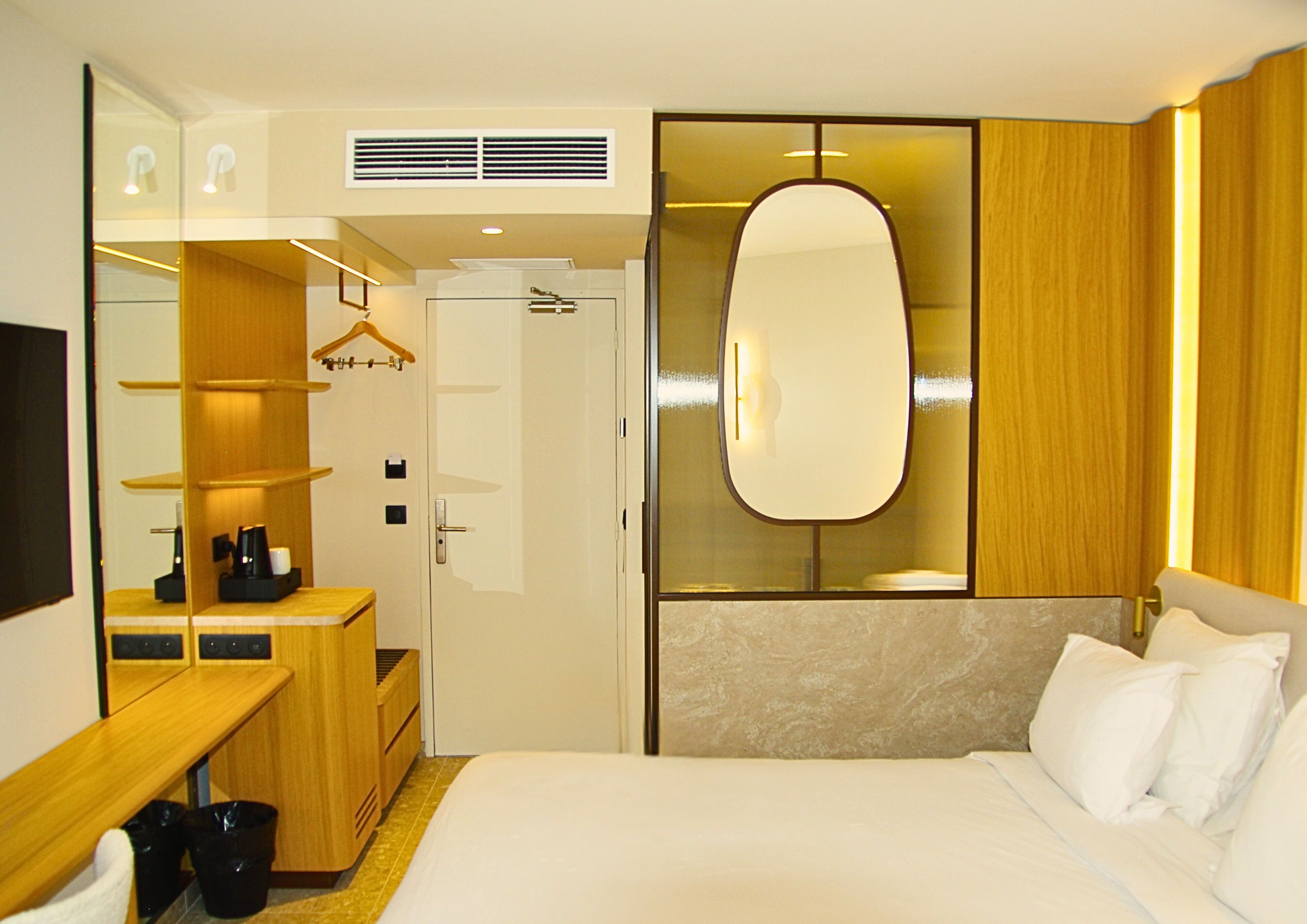 Una habitación de hotel con cama, escritorio con cafetera, espejo y armario.