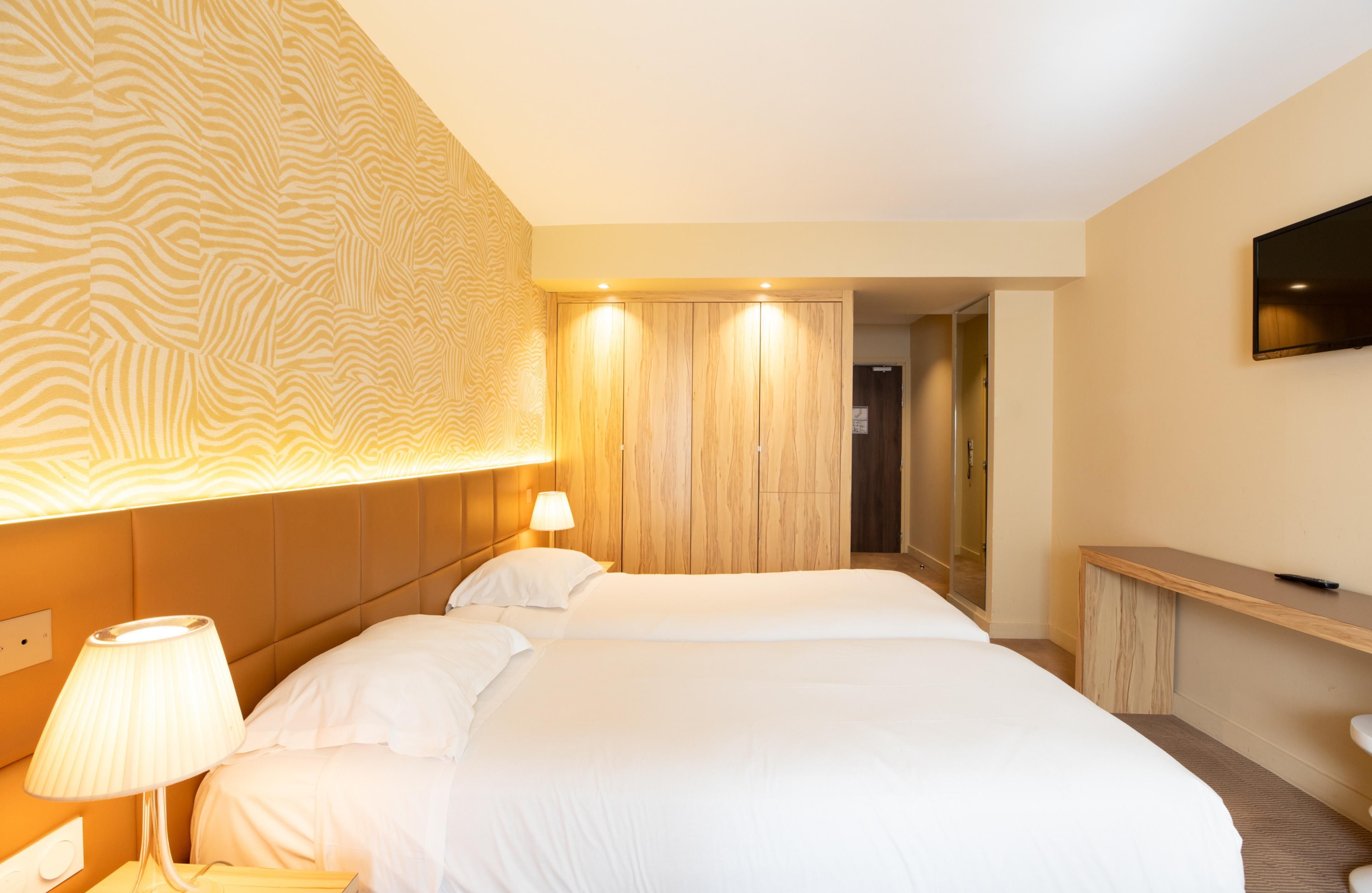 Een hotelkamer met een groot bed, een bedlampje, een aan de muur bevestigde televisie en een houten garderobe.