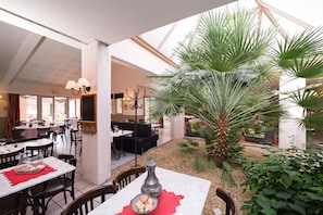 Enjoy meals in a spacious dining area with a high ceiling, lush greenery, and comfortable seating options.