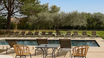 Zona de piscina con sillones de playa, una mesa y sillas de mimbre.