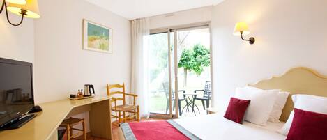 A hotel room with a bed, a desk, a chair, a television, and a window with a view of greenery.