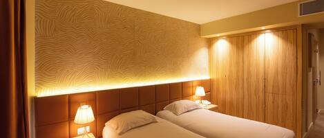 Una habitación de hotel con dos camas, cabecera con diseño estampado, lámparas de noche y un armario de madera.