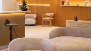 A modern living room with a sofa, chairs, a coffee table, and a reception area with a counter and shelves. - Golden Tulip Avignon Le Paradou (Avignon)