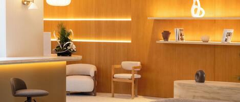 A modern living room with a sofa, chairs, a coffee table, and a reception area with a counter and shelves.
