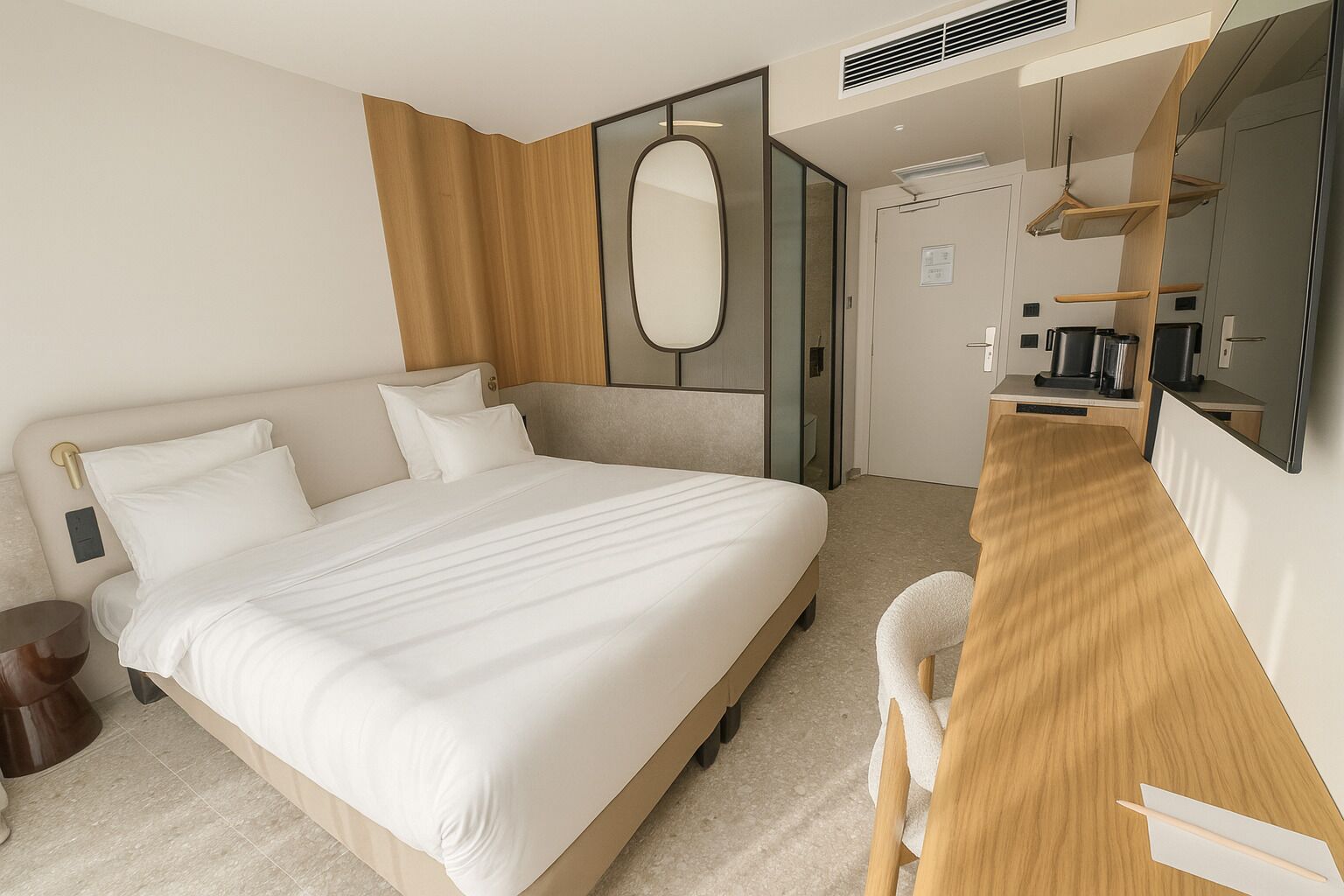 Una camera d'albergo moderna con un letto grande, una scrivania in legno, uno specchio e una macchina per il caffè.