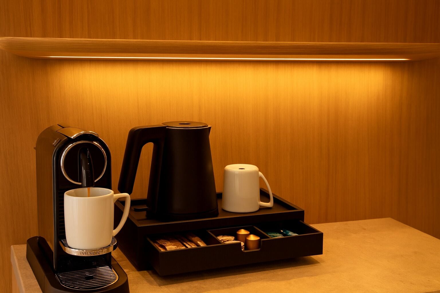 Un coin café équipé d’une machine à café, d’une bouilloire, d’une tasse et d’un plateau contenant des sachets de thé et un briquet.