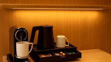 Un coin café équipé d’une machine à café, d’une bouilloire, d’une tasse et d’un plateau contenant des sachets de thé et un briquet.