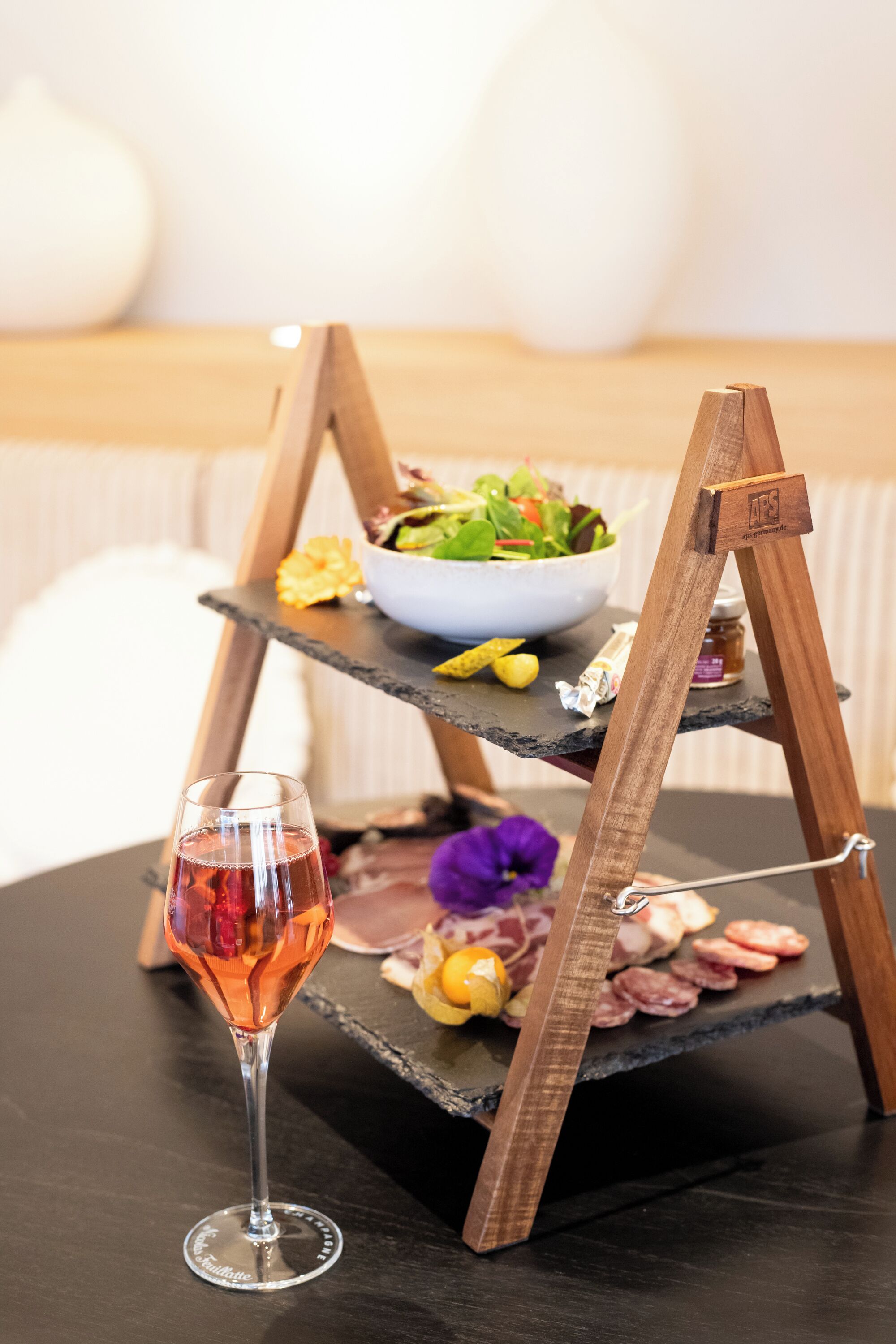 A wooden stand with a bowl of salad, a glass of red drink, and some food items on a dark surface.