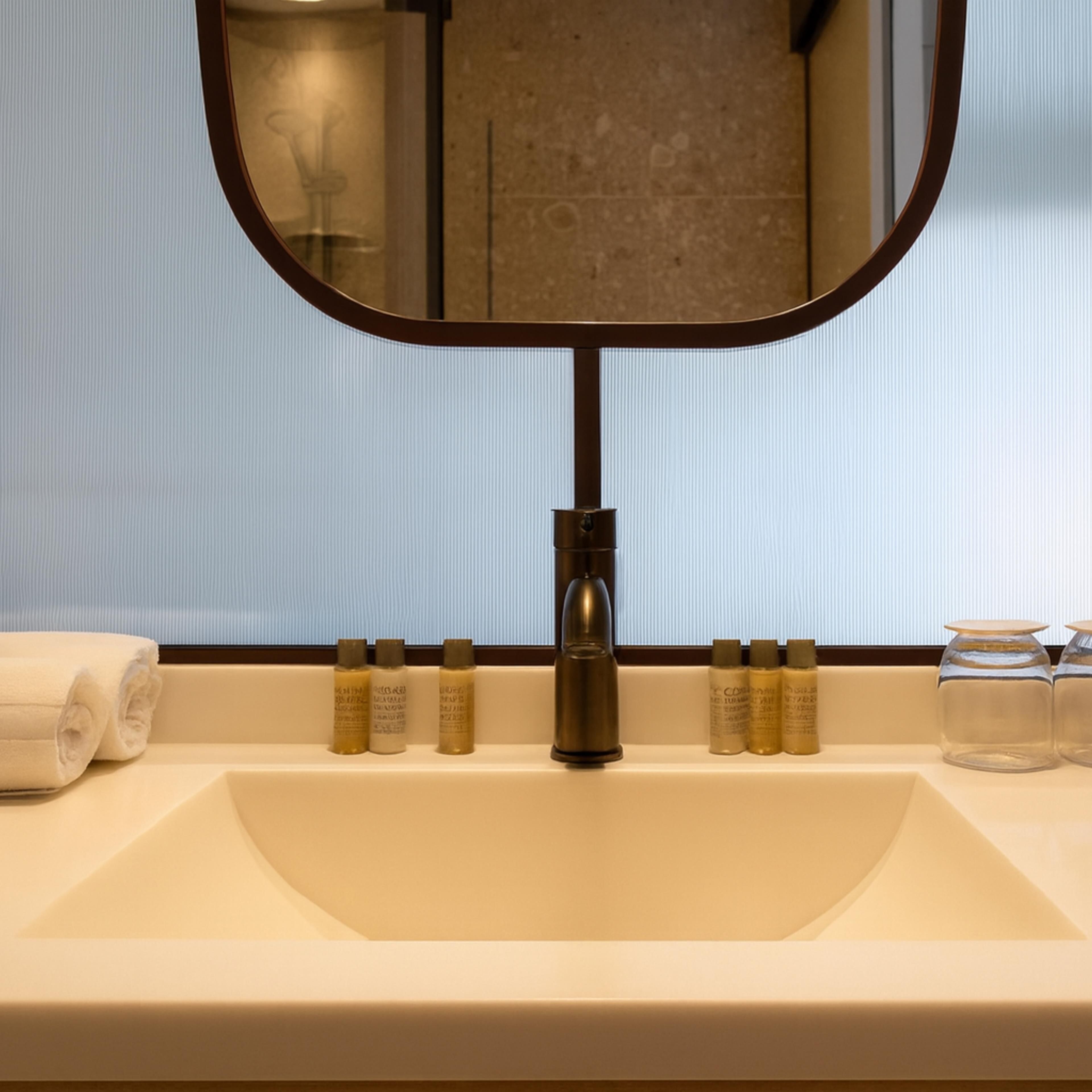 Ein Badezimmerwaschbecken mit Spiegel, Handtuch und Toilettenartikeln.
