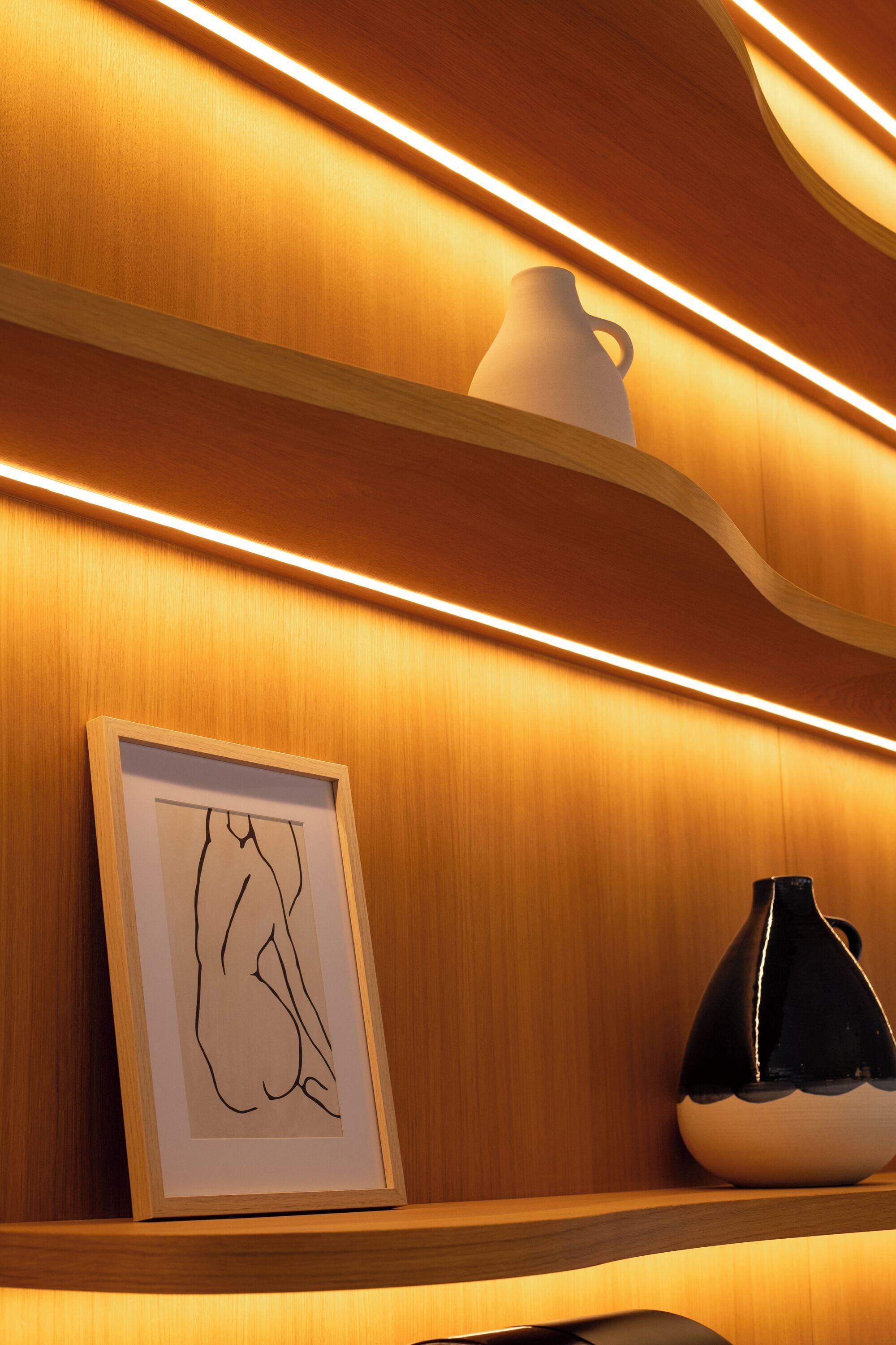 A wooden wall with a framed artwork and a black and white vase on a shelf.