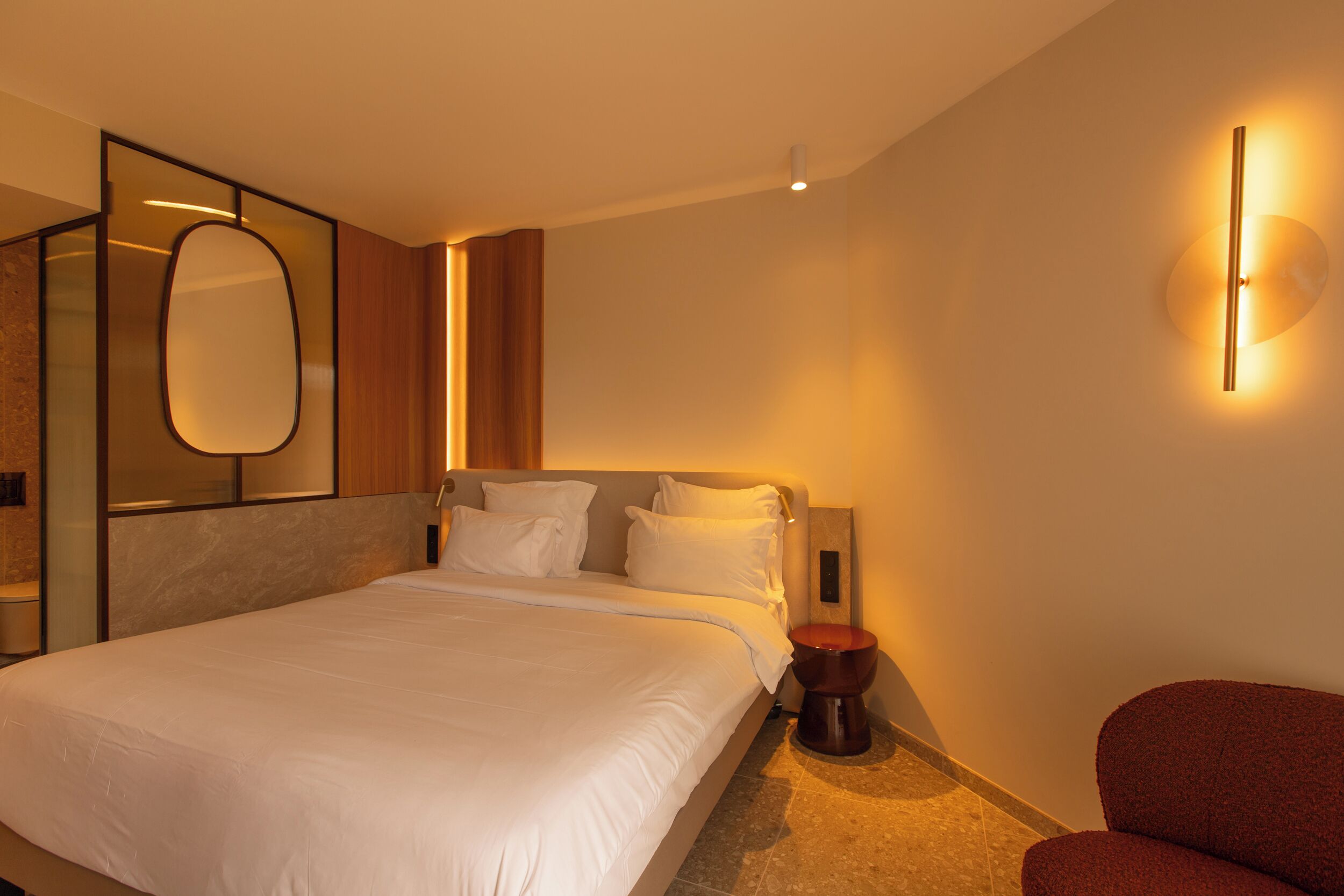 A hotel room with a large bed, a wooden headboard, a round side table, and a red armchair.