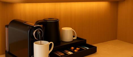 Una màquina de cafè amb una tassa i un safata de càpsules de cafè damunt un taulell.