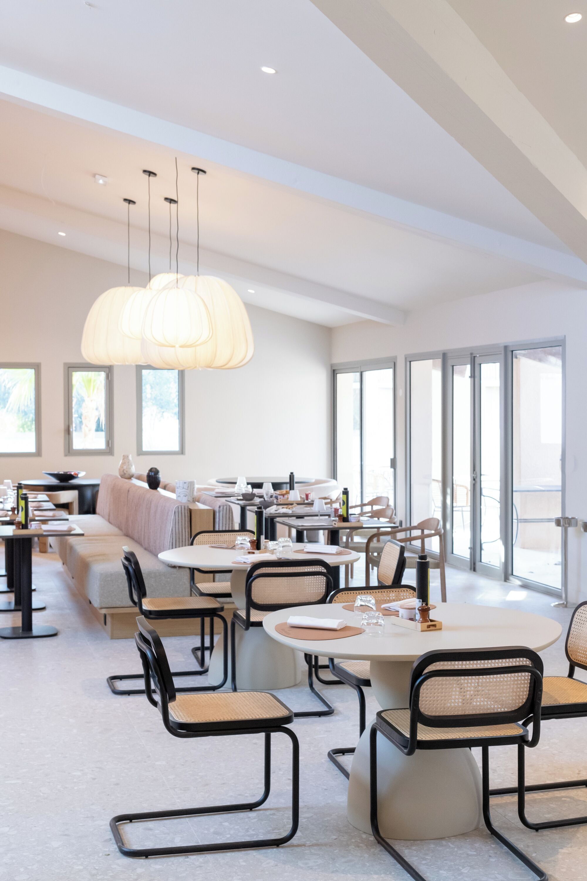 Un comedor moderno con mesas redondas, sillas de metal negro e iluminación colgante.