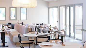 A modern dining area with round tables, black metal chairs, and pendant lighting.