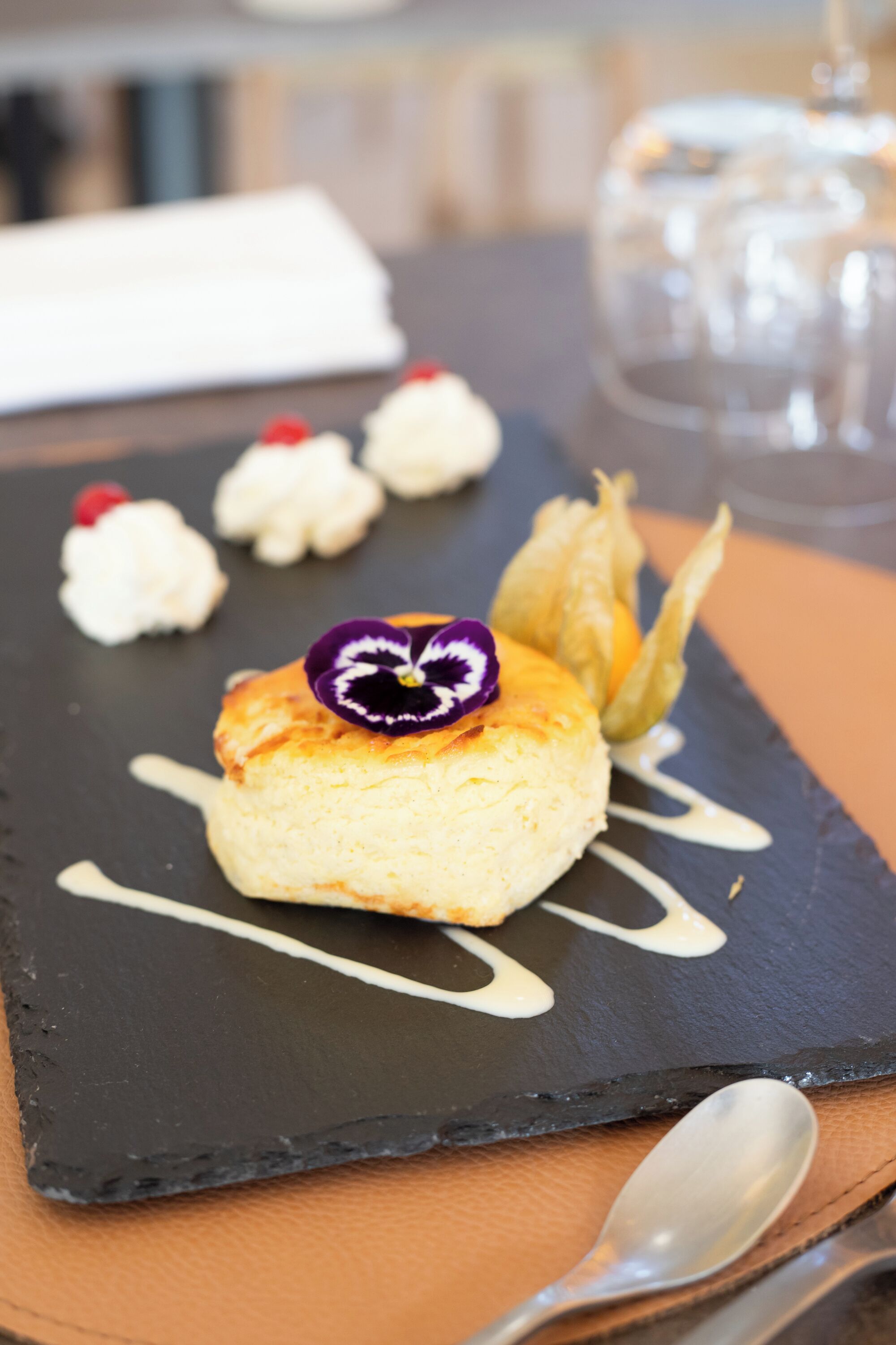Une assiette à dessert avec une pâtisserie, une fleur et de la crème fouettée, le tout présenté sur une planche d'ardoise.
