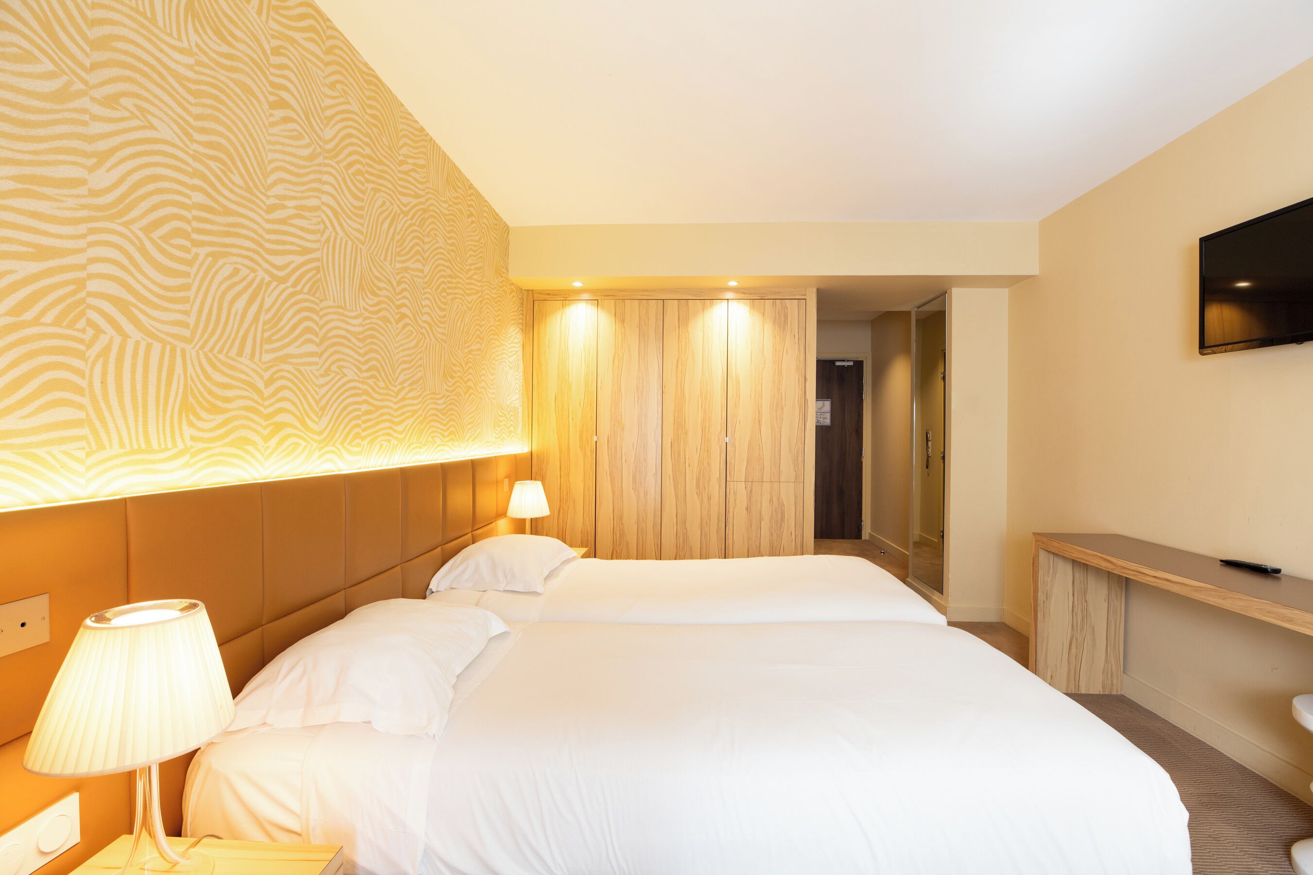 Une chambre d’hôtel avec un grand lit, une lampe de chevet, un téléviseur fixé au mur et un mur décoré de panneaux en bois.