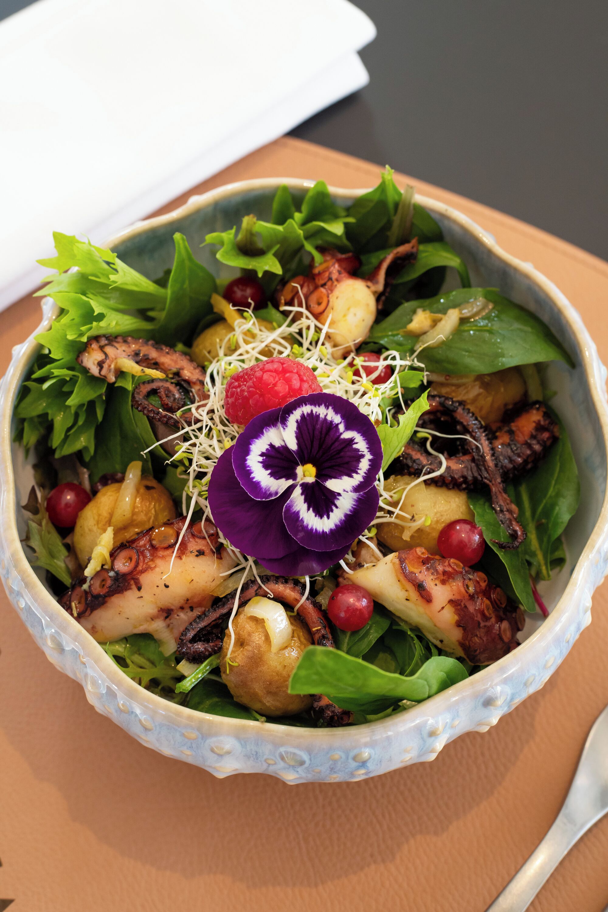 A bowl of salad with various greens, octopus, and garnishes.