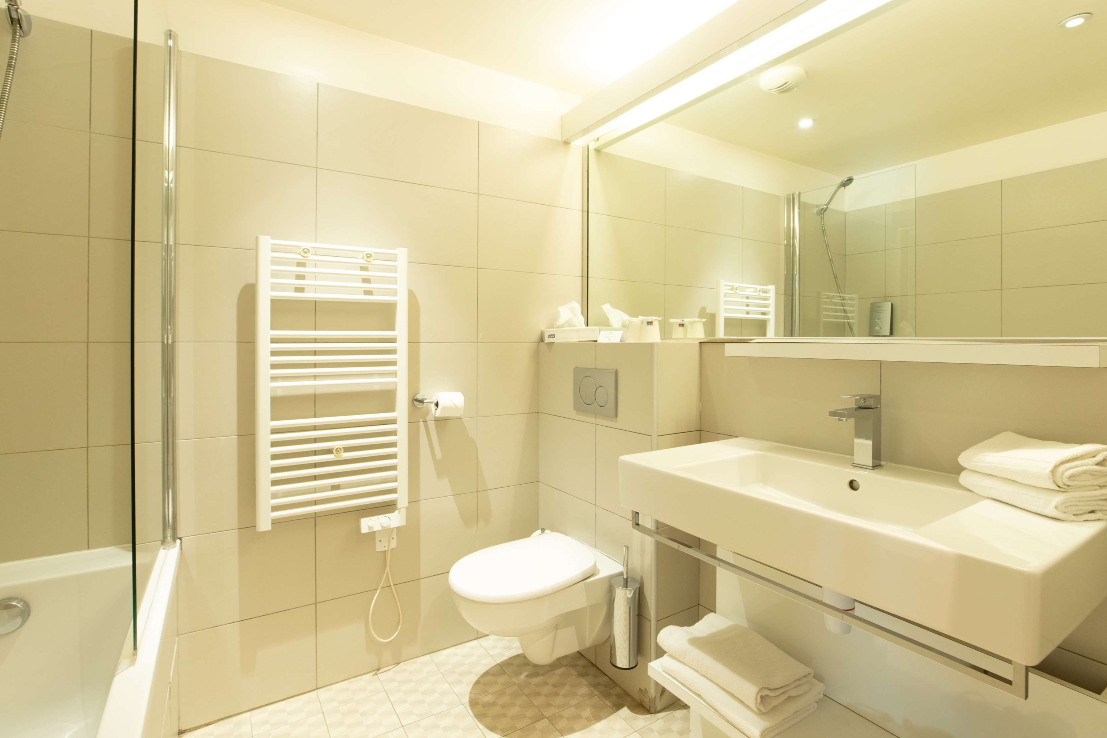 Une salle de bain moderne avec une douche à parois de verre, des toilettes blanches, un meuble-lavabo avec un miroir et un porte-serviettes.