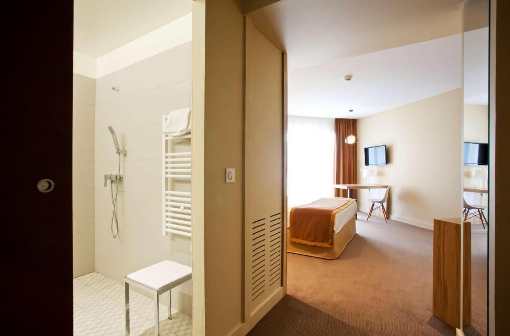 A hotel room with a shower, a bed, a desk, and a TV.