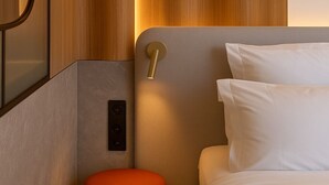 A modern hotel room with a wooden panel wall, a red ottoman, a bed with white linens, and a wall-mounted light fixture. - Golden Tulip Avignon Le Paradou (Avignon)