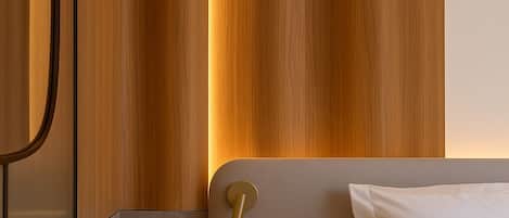 A modern hotel room with a wooden panel wall, a red ottoman, a bed with white linens, and a wall-mounted light fixture.