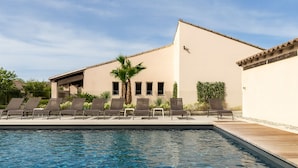 A swimming pool with lounge chairs, a palm tree, and a building with windows and a flat roof. - Golden Tulip Avignon Le Paradou (Avignon)