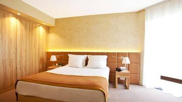A hotel room with a large bed, two bedside tables, a headboard with a textured pattern, and a wooden wardrobe.