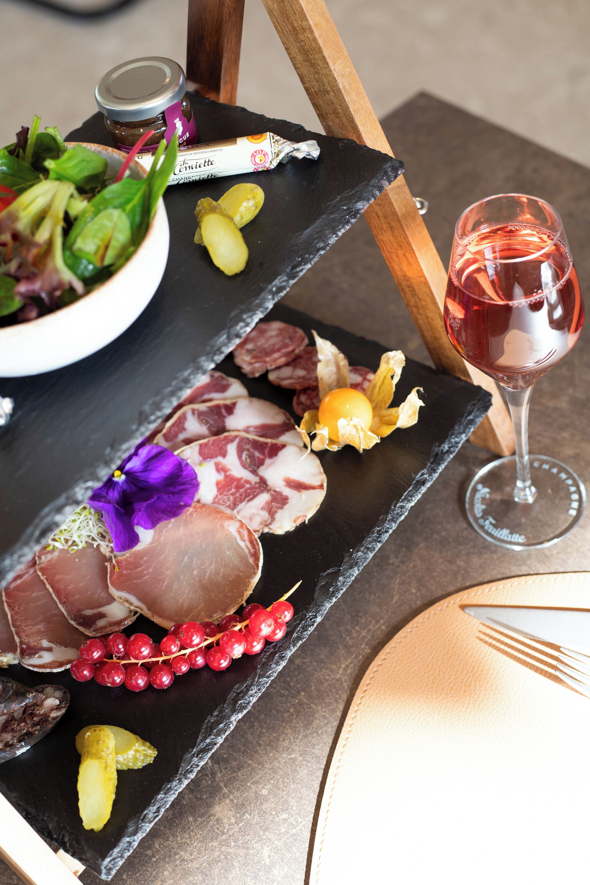 A slate serving board with various food items, a glass of red wine, and a bowl of salad.