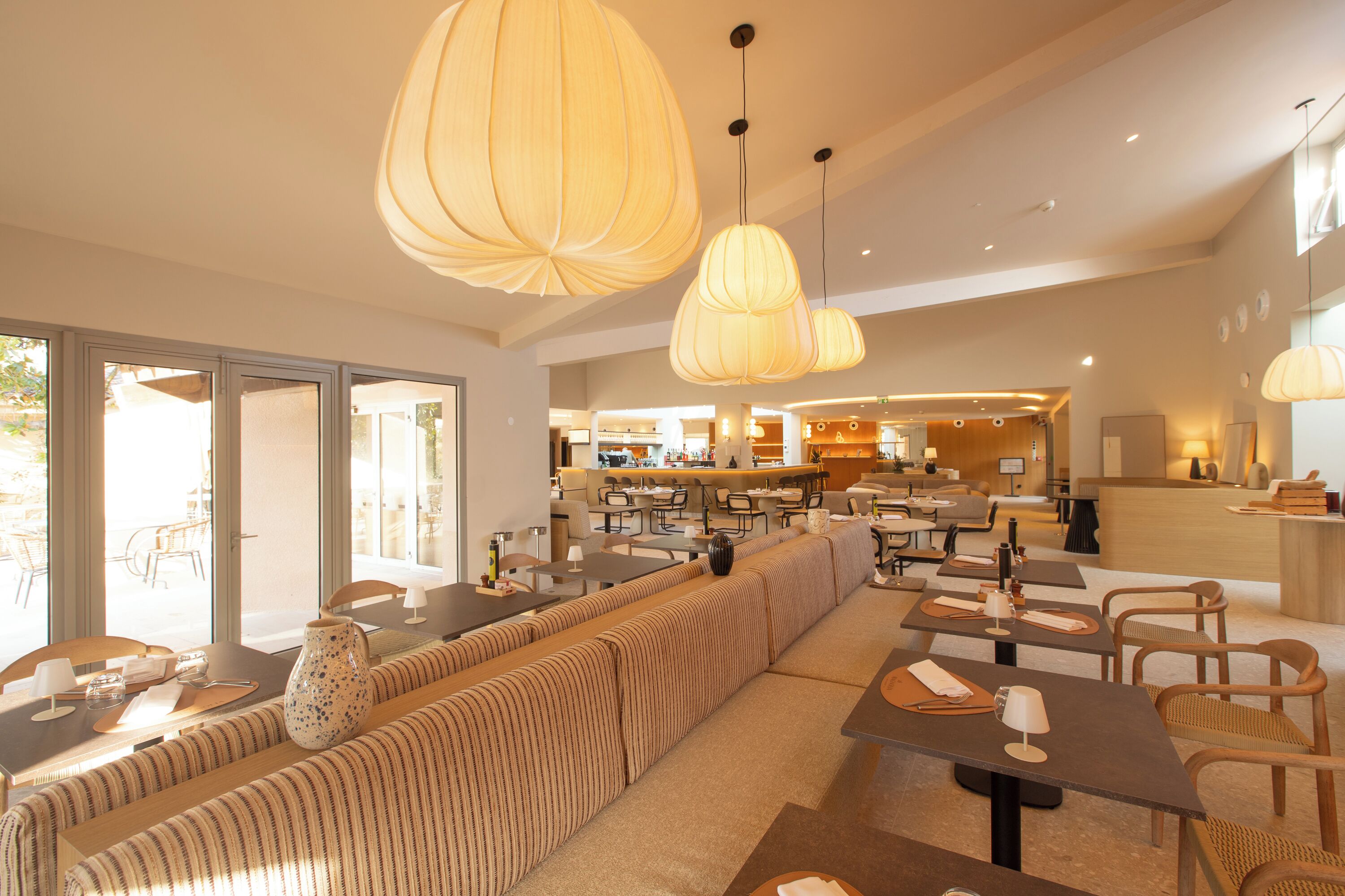 Un hall d’hôtel moderne doté d’un grand espace salon, de tables à manger et de luminaires suspendus.