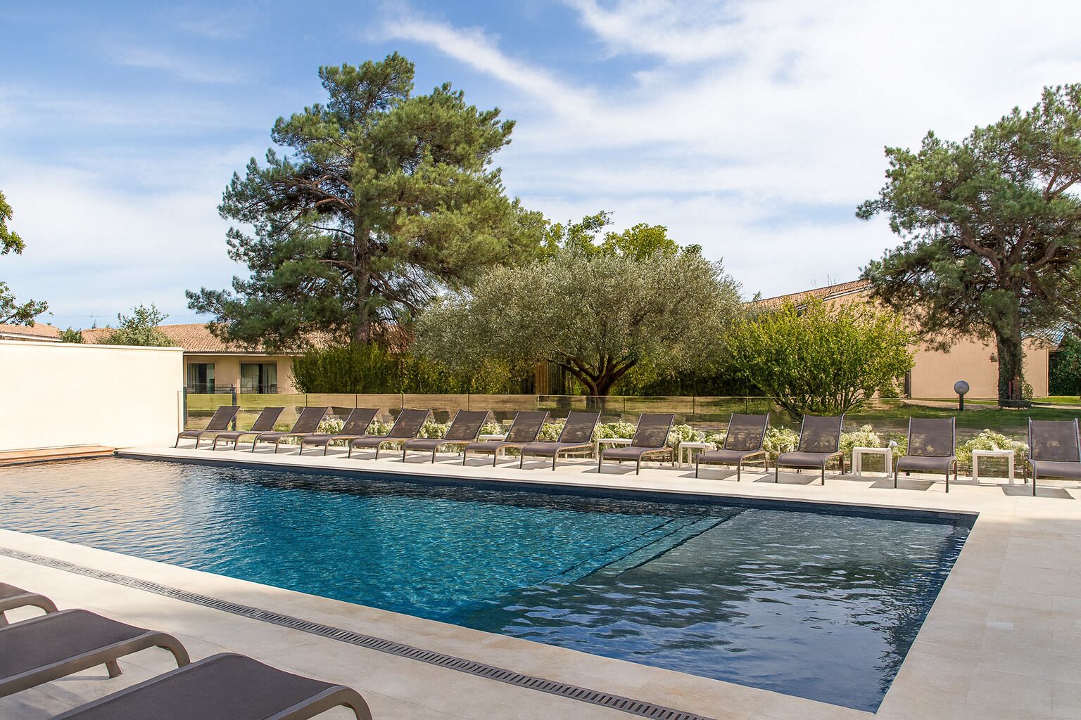 A rectangular swimming pool with a tiled deck, surrounded by lounge chairs and trees.