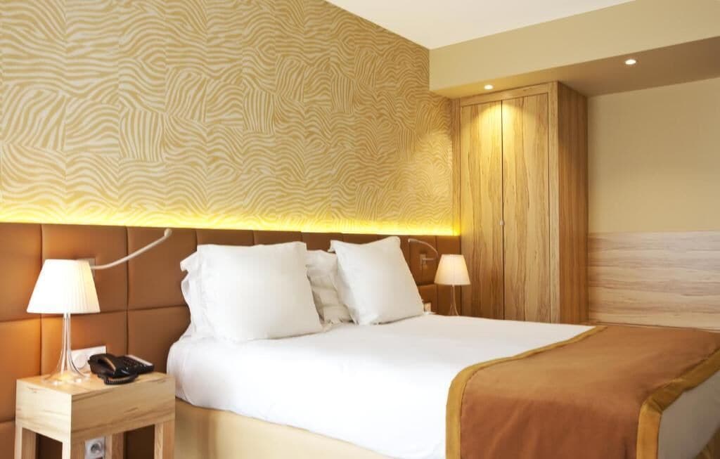 Une chambre d’hôtel avec un grand lit, deux tables de chevet avec des lampes, une armoire en bois et un mur décoré d’un motif.