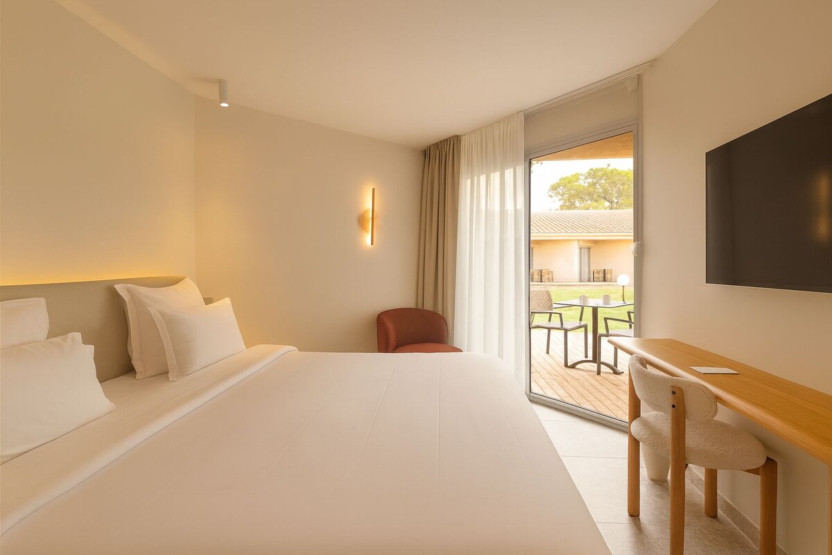 Habitación de hotel con una cama grande, un escritorio con silla, televisor y vistas al exterior.