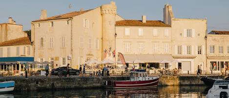 A waterfront hotel with a boat docked in front, outdoor seating, and a view of the water.