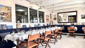 A restaurant interior with multiple tables, chairs, and a large window overlooking the street. - Hotel de Toiras (Saint-Martin-de-Re)