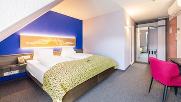 A hotel room with a bed, a desk, a chair, and a phone on the nightstand.