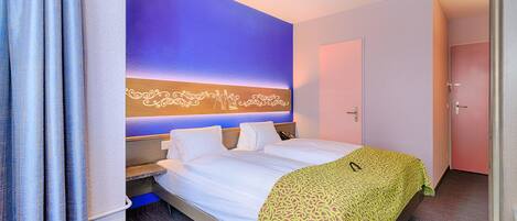 A hotel room with a bed, a nightstand, a wall-mounted light, and a door.