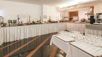 A buffet setup with a variety of food items and beverages, a coffee machine, and a large number of wine glasses arranged on tables.