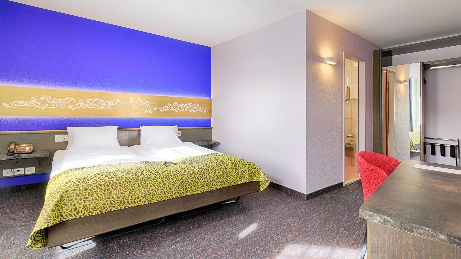 A hotel room with a bed, bedside table, and a red chair.